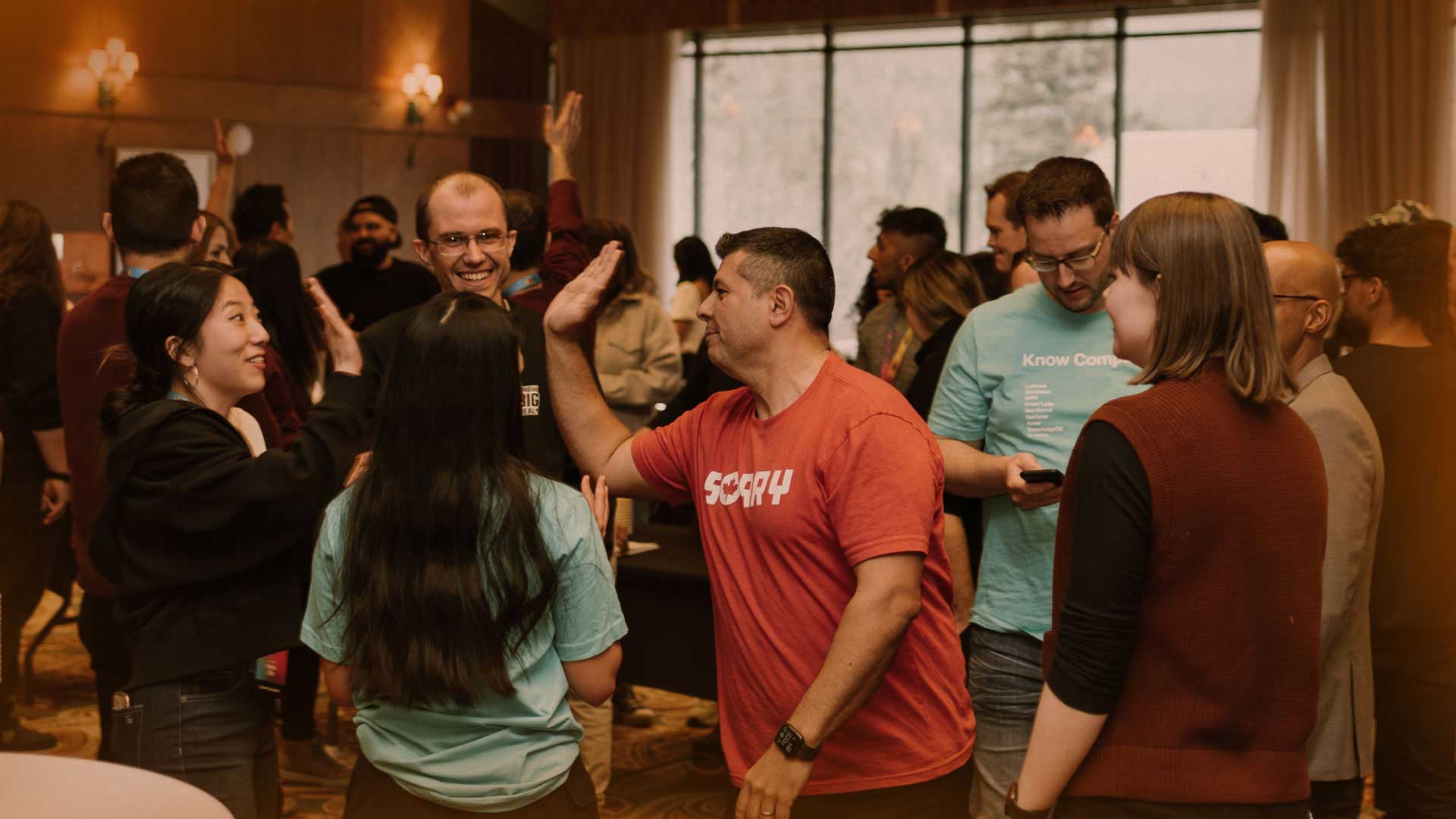 A photo of a two Know Company employees high-fiving surrounded by other employees.